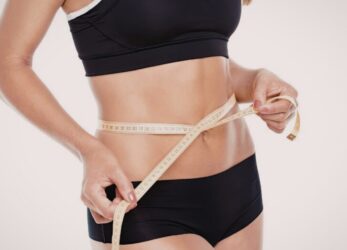 Woman measuring her waist using a measuring tape to signify weight loss