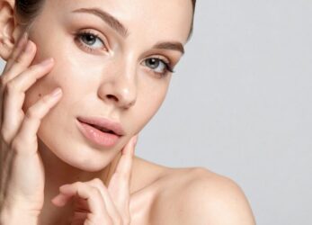 Close up of a woman gently touching the sides of her face against a neutral background