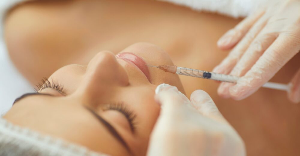 A gloved hand administering an injection near a person's lips as they lie down with eyes closed