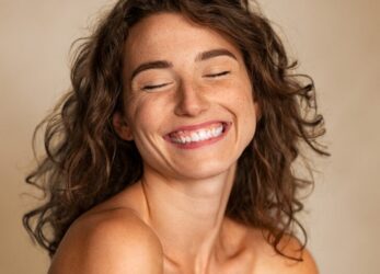 Woman with freckles smiling with her eyes closed against a neutral background